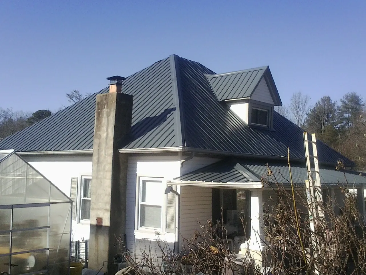 Dark blue standing seam metal roof on a white farmhouse with dormer — Slate & Tile Roof Repair by Roofing Brothers in Edmond