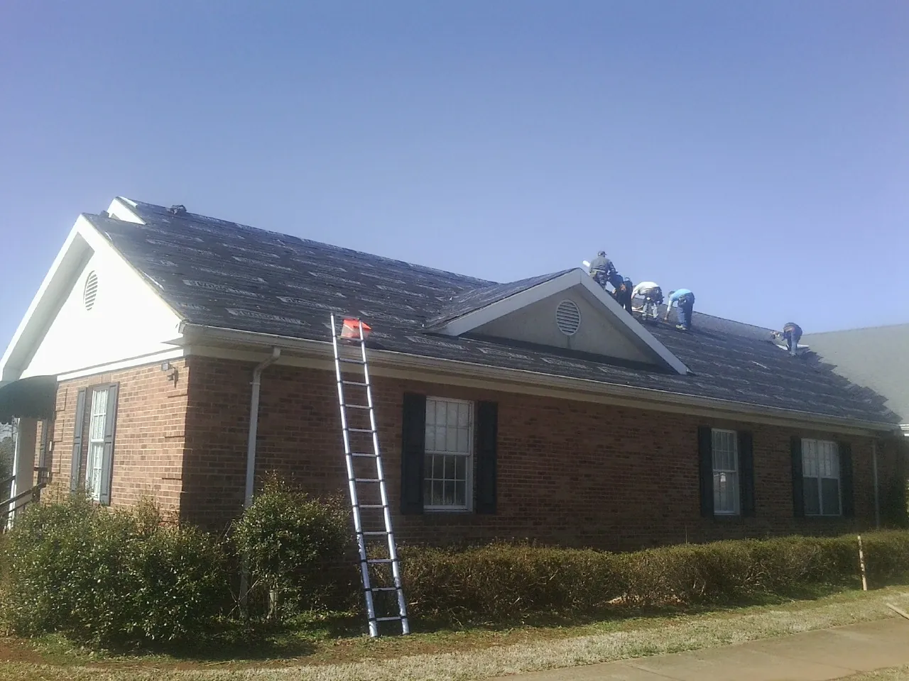 Crew tearing shingles off a brick ranch roof with a ladder set — Metal Roof Repair work by our crew in Edmond