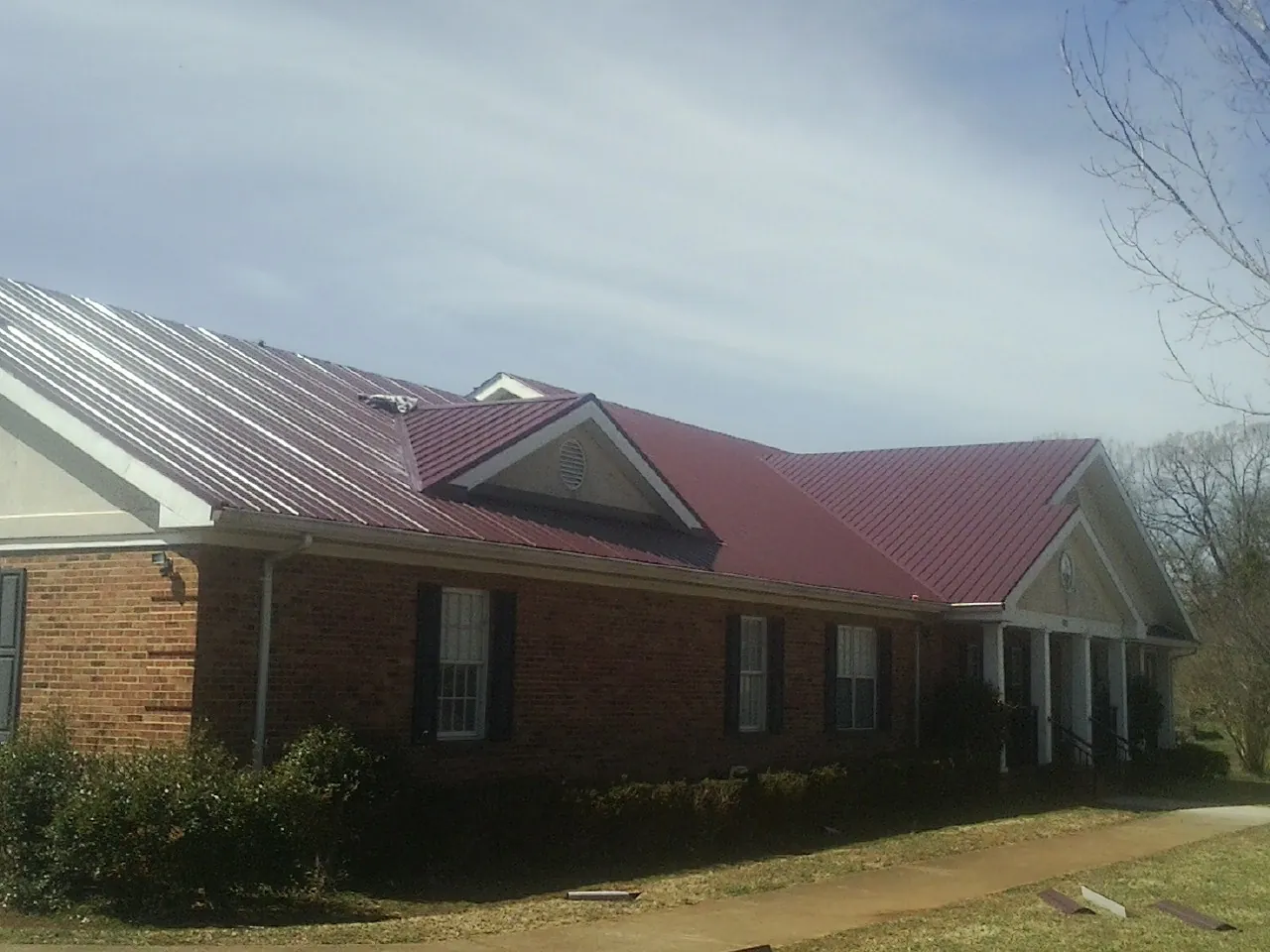 Red metal roof with gabled entries on a long brick building, from a Hail Damage Roof Repair job in Edmond