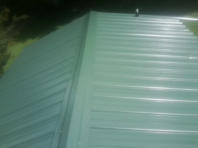 New green metal panels meeting at the ridge of a roof — Flat Roof Repair work by our crew in Edmond