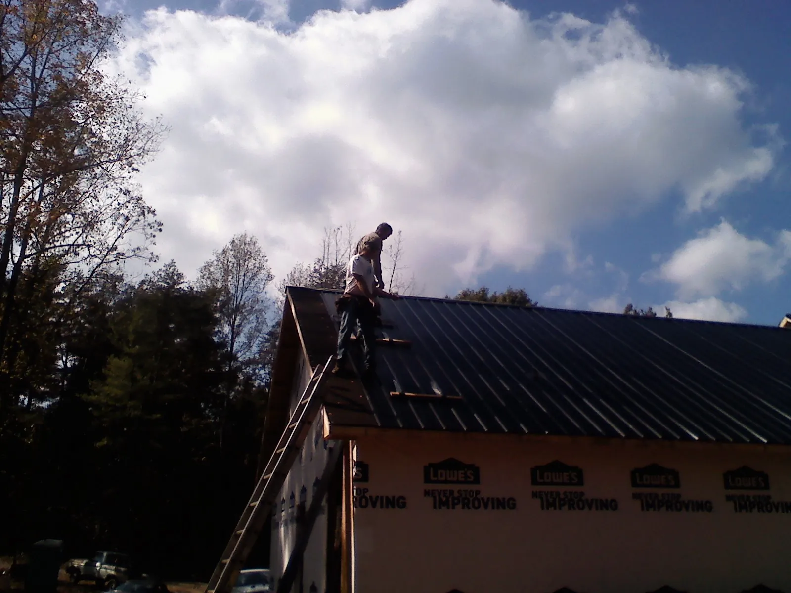 Roofer fastening dark metal panels high against a cloudy sky, from a Roof Inspection job in Edmond
