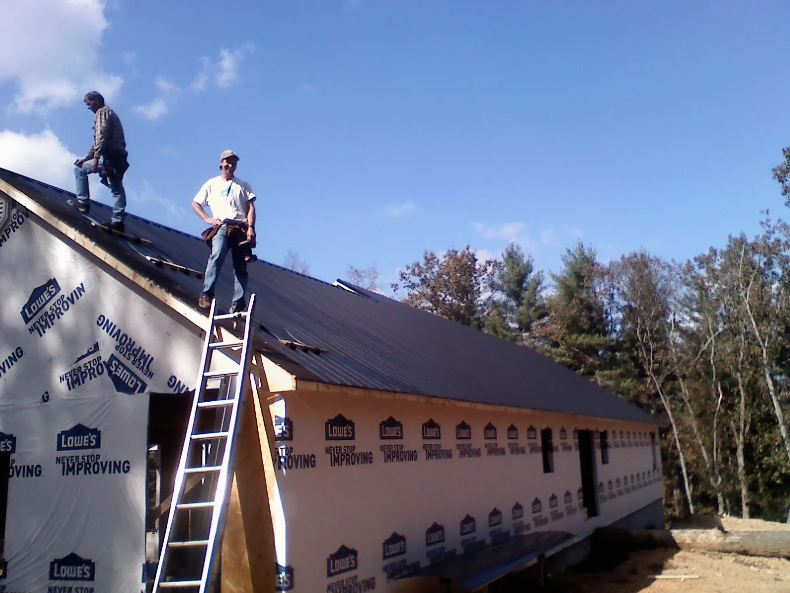 Two roofers standing on a long dark metal roof over a wrapped building in Edmond