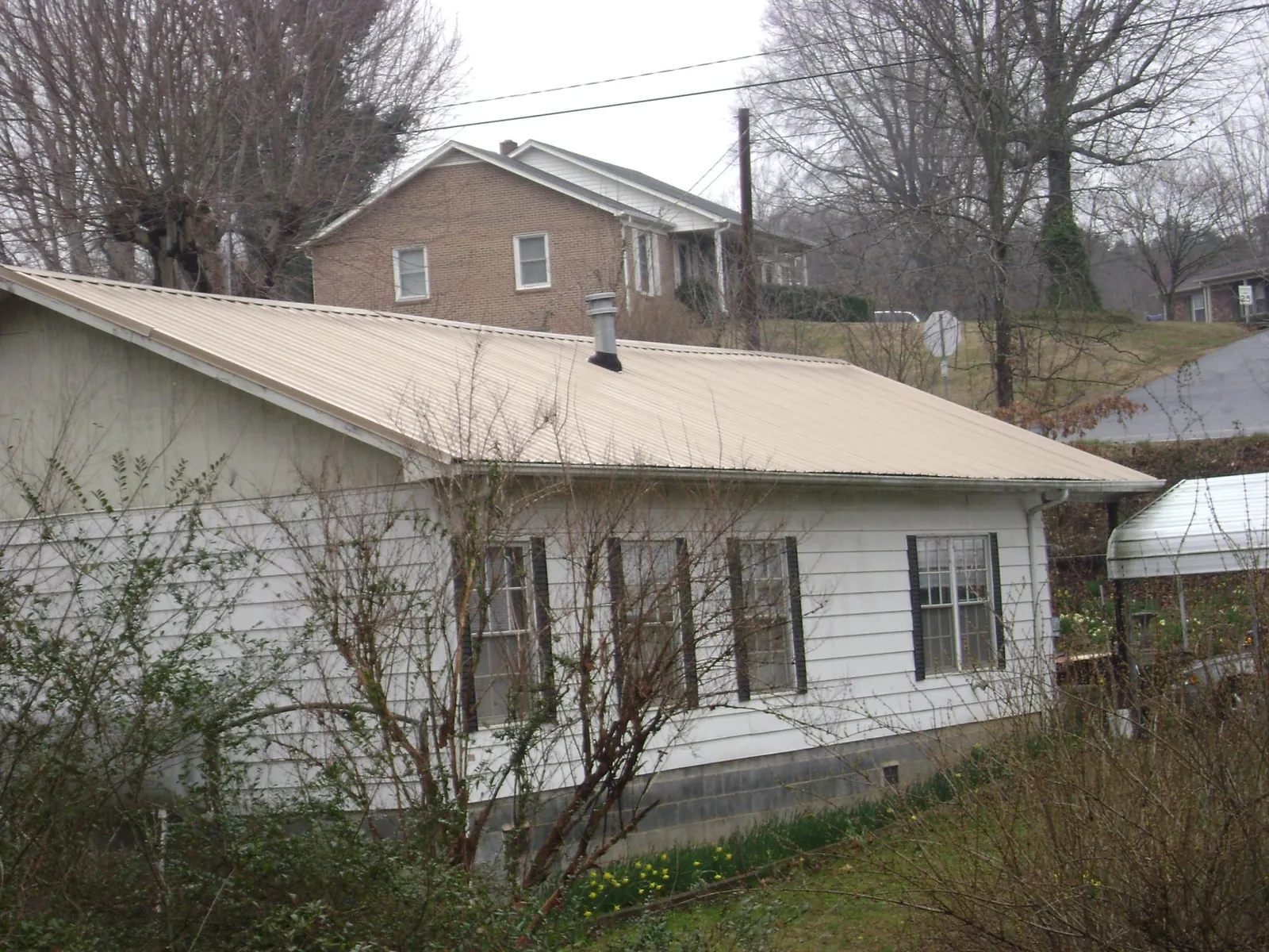 Tan metal roof on a white sided house set into a hillside — Commercial Roofing by Roofing Brothers in Edmond