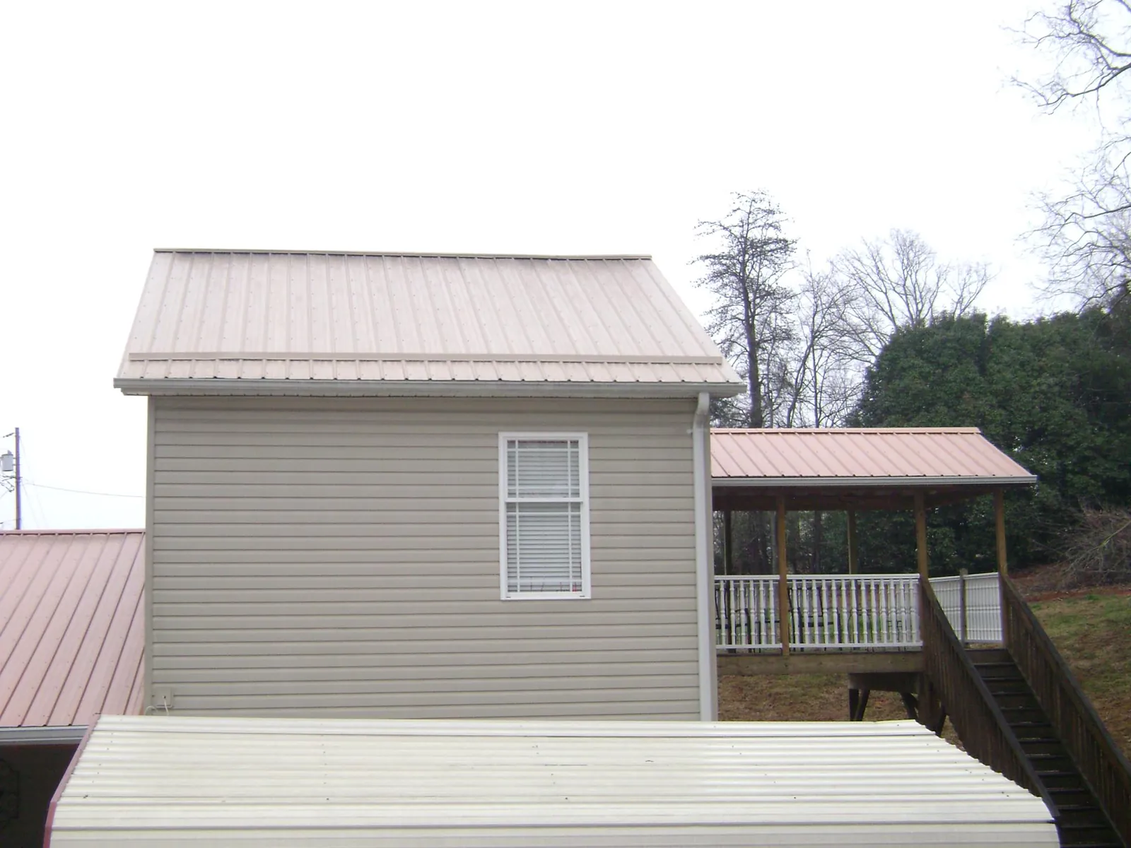 Tan metal roofs on a two story addition and attached porch, from a Roof Replacement job in Edmond